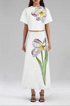Woman wearing a white outfit with floral designs on a plain background